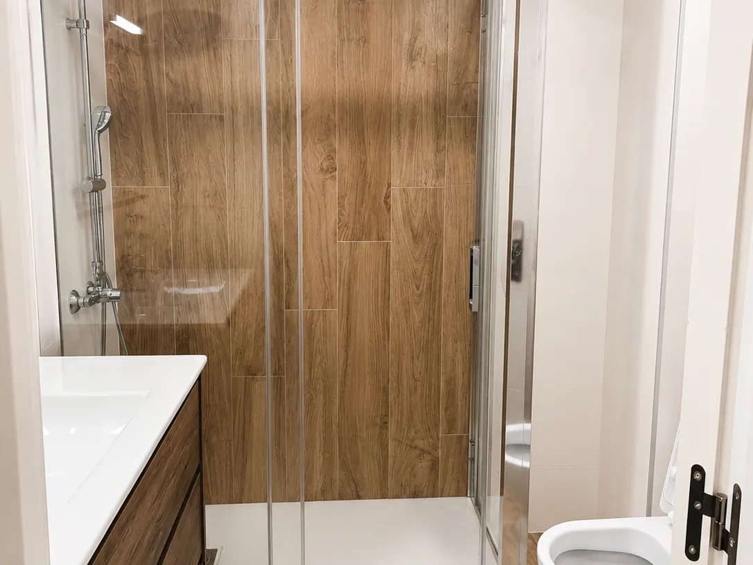 Vista frontal de ducha con mampara de cristal y revestimiento efecto madera en reforma de bano en Valencia