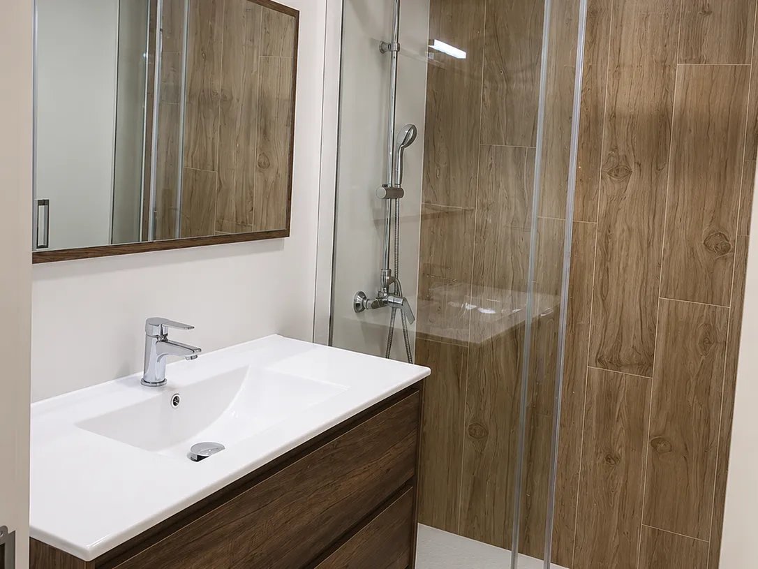 Bano en Valencia con mueble suspendido de madera, ducha con mampara frontal y revestimiento efecto madera